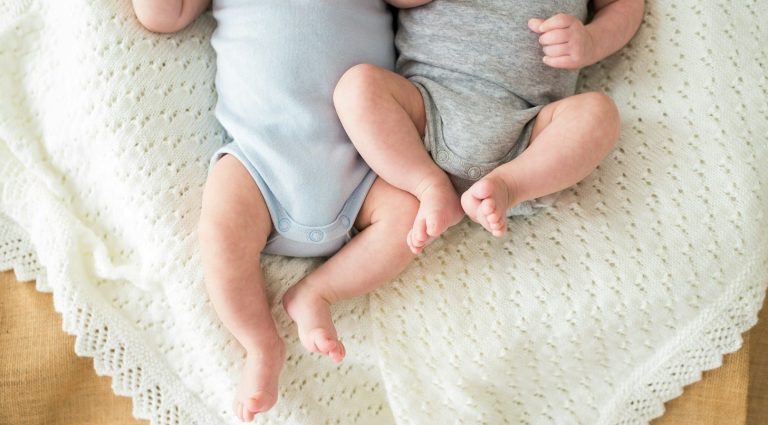 Zwillinge die Strampeln Zwei Babys in bodenlangen Stramplern liegen auf einer weichen Decke.