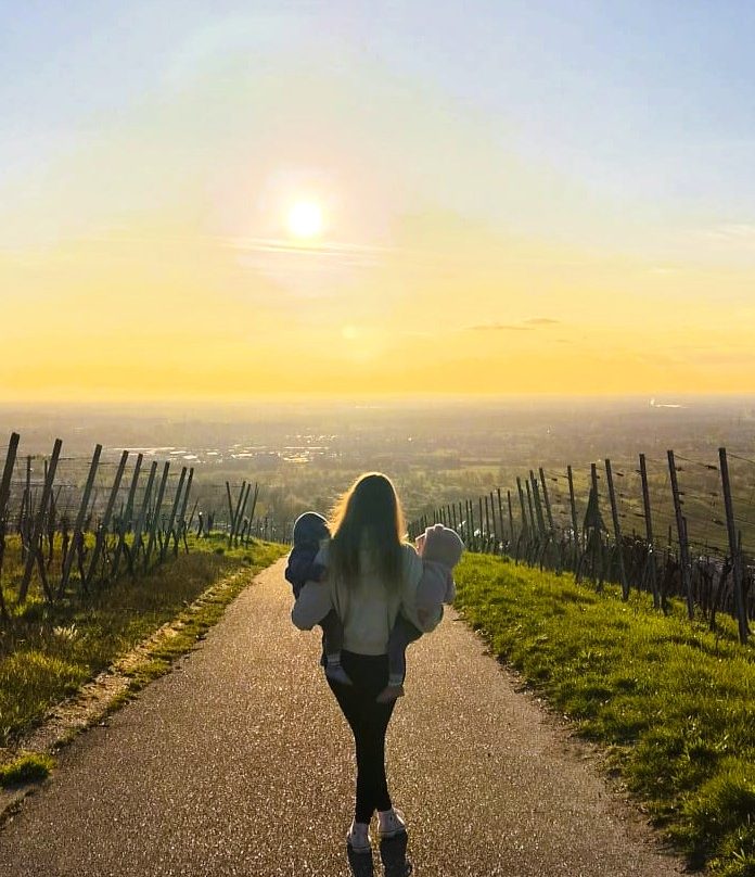 Mutter mit Zwillingen Eine Person geht einen Weg durch Weinberge bei Sonnenuntergang.