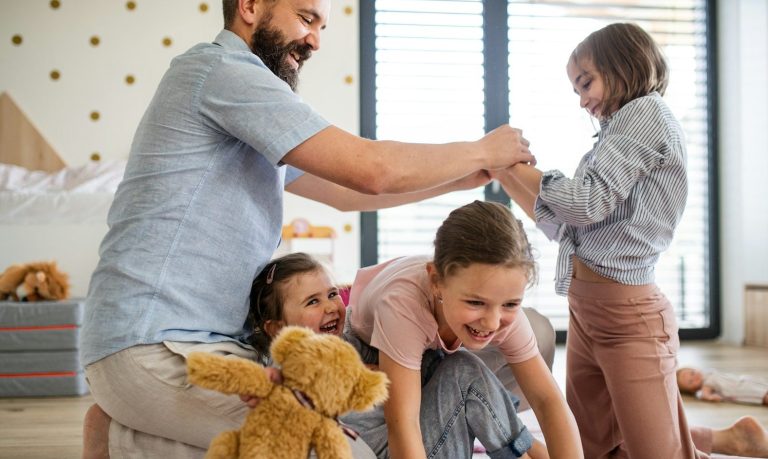 Papa mit Drillingskindern Ein Mann spielt mit vier Kindern im Raum, während sie lachen und spielen.