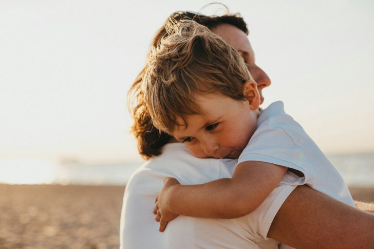 Mutter mit Kind Eine Mutter umarmt ihr kleines Kind am Strand bei Sonnenuntergang.