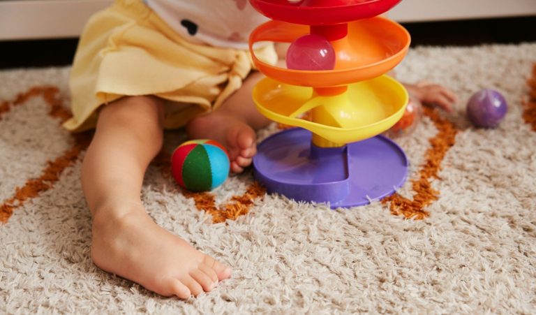 Kind und Bällebahn Ein kleines Kind spielt mit bunten Stapeltürmen auf einem weichen Teppich.