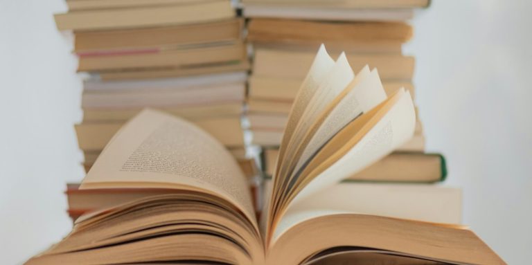 Bücher Offene Bücher vor einem Stapel geschlossener Bücher auf einem hellen Hintergrund.